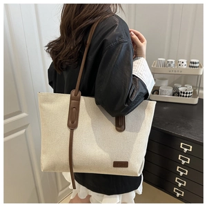 Detail view of large beige canvas tote bag with brown leather straps and fashion label