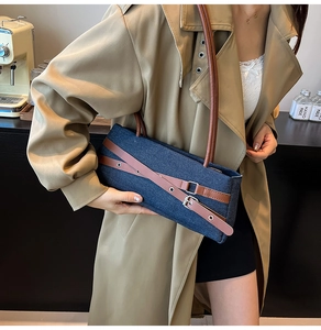 Detailed shot of denim baguette bag with brown leather straps and metal buckle accents