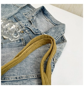 Detail of khaki corduroy strap over light blue washed denim jacket with metal button