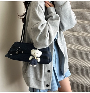 Close-up of blue denim shoulder bag featuring leather buckles and cute white plush bear charm