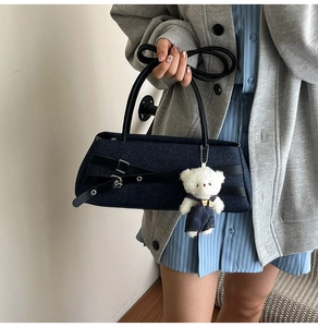Detail of dark blue denim handbag featuring a cute bear charm and black strap detail