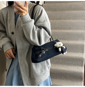 Detail of dark blue denim shoulder bag featuring black leather straps and plush bear charm