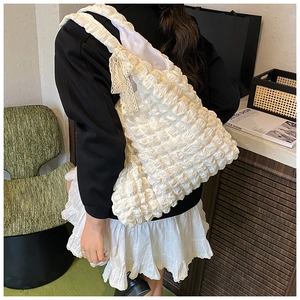 Detail of white bubble pleated tote bag featuring lace bow and textured shoulder strap