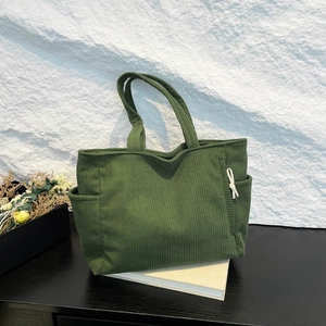 Dark green corduroy tote bag with side pockets and knot detail in a minimalist scene