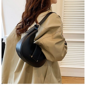 Detail of a black crescent shoulder bag featuring light gold metal buckle on leather