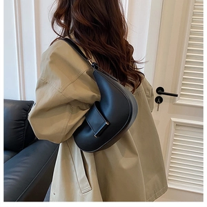 Detail of a black crescent shoulder bag featuring a sleek leather texture and square buckle