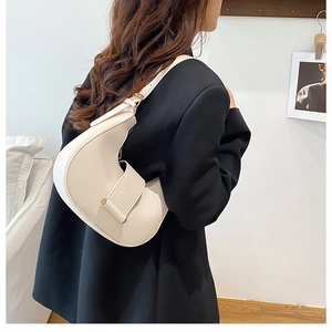 Side view of an off-white half-moon shoulder bag worn by a model in a minimalist room