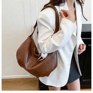 Detailansicht einer braunen Hobo-Tasche mit weißem Plüsch-Anhänger und eleganter PU-Struktur