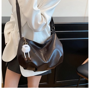 Nahaufnahme der braunen Hobo-Tasche aus Leder mit breitem Gurt und weißem Plüsch-Anhänger