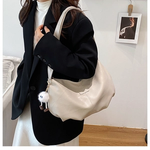 Beigefarbene Hobo-Tasche mit Plüsch-Anhänger getragen von einem Modell im Büro
