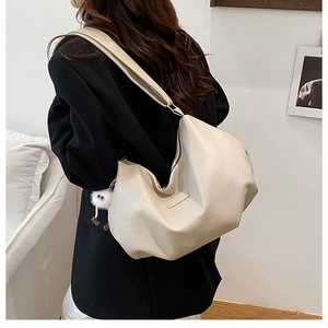 Detailansicht der cremeweißen Oversize-Beuteltasche mit flauschigem Monster-Anhänger