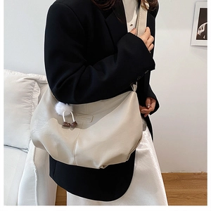 Détail d'un sac bandoulière beige en similicuir avec pompon blanc porté sur veste noire