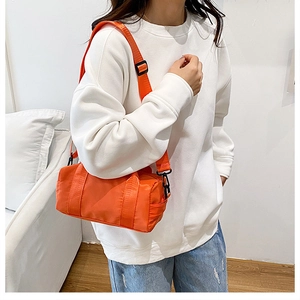 Detail view of orange cylindrical nylon crossbody bag with adjustable textile shoulder strap