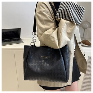 Close-up of black quilted tote bag with chain strap and brand logo on leather surface