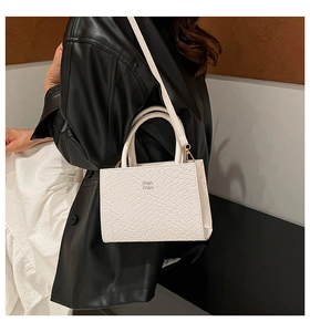 Close-up of white embossed leather crossbody bag with top handle and logo detail