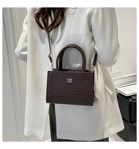 Detail shot of the woven texture and metal logo on a coffee brown crossbody handbag