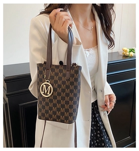 Close-up of brown monogram crossbody bag with golden M pendant on white blazer
