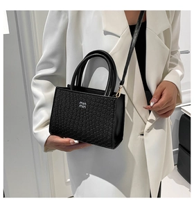 Detail of black faux crocodile leather handbag with metal logo and woven texture finish