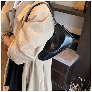 Detailed close-up of a black glossy underarm bag showing the sleek leather texture