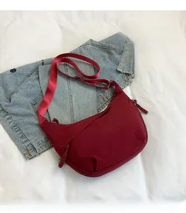 Close-up of wine red nylon crescent bag on denim background with adjustable strap