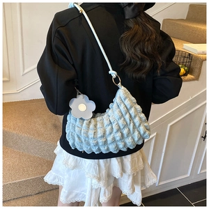 Détail de la texture plissée bleu clair et du charme de fleur blanche sur le sac bandoulière