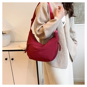 Side view of burgundy nylon crescent bag with adjustable strap on a female model