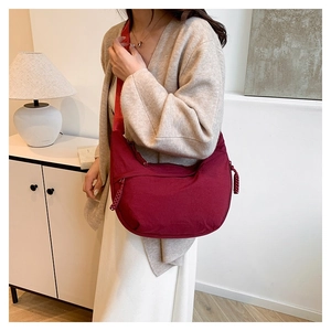 Model wearing a burgundy crescent nylon crossbody bag in a cozy home setting