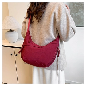 Detail of burgundy nylon crescent bag showing the woven zipper pull and crossbody fit