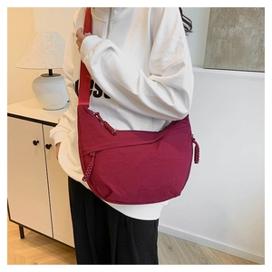 Detail of burgundy nylon crescent bag with layered zipper pockets and woven puller