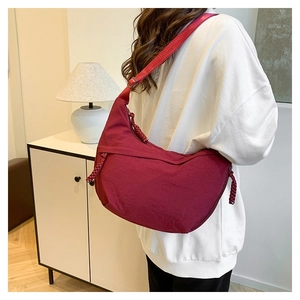 Detail of burgundy nylon crescent bag showing the adjustable strap and woven zipper pull
