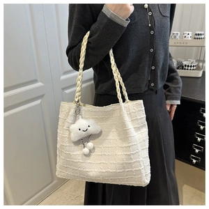 Detail of cream-white tweed tote bag with braided handles and cloud charm in a home setting