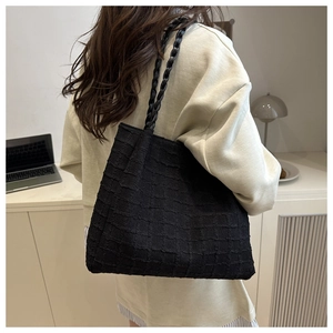 Detailed view of black textured tote bag with woven shoulder straps in casual lifestyle setting