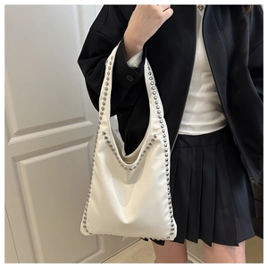 Detail of white leather tote bag with silver rivets worn by a model in a black outfit