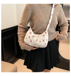 Detail of white corduroy hobo bag with red cherry prints worn over the shoulder