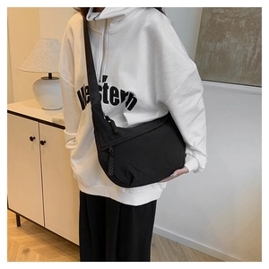 Close-up of a black nylon crescent crossbody bag worn by a model in a modern home setting