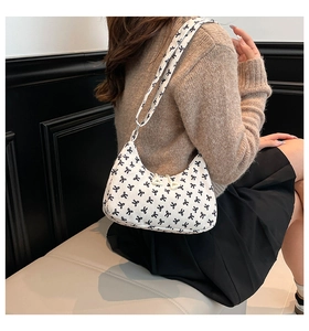 Detail of stylish shoulder bag with bow print worn over oatmeal knit sweater