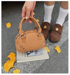 Detail of a brown suede rivet crossbody bag on a book with autumn leaves