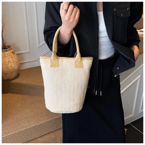 Detail of hand-woven beige bucket bag with yellow straps shown in a minimalist setting