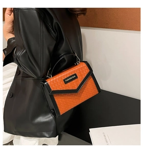 Detail of woven texture flap bag in orange and black with metal handle and label