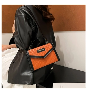 Close-up of an orange woven leather handbag with black trim held by a model in a leather jacket