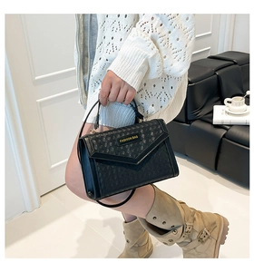 Detail of black woven crossbody bag with V-shaped envelope flap and gold metal logo