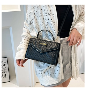 Close-up of black woven texture handbag with gold fashion tag and crossbody strap