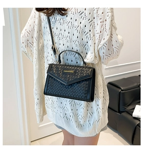 Detail of black woven crossbody bag with gold metal logo and envelope flap closure