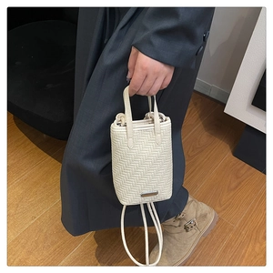 Detail view of cream woven crossbody phone bag with handle and metal logo plate