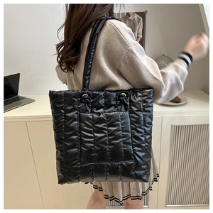 Detail of a black quilted tote bag showing high-gloss padded texture and a front pocket