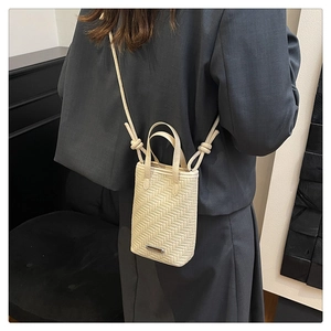 Close-up of a cream woven crossbody phone bag with knot strap and metallic bar detail