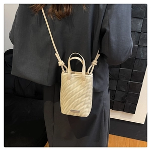 Detail of cream woven mini crossbody bag showing texture and knotted strap design