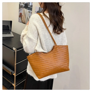 Detail view of brown woven leather tote bag worn by a model in a natural office setting