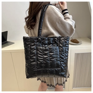 Quilted black puffer tote bag shown on shoulder in a stylish minimalist interior setting