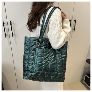 Detail view of large dark green quilted down tote bag with metallic finish on model